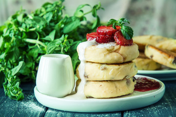 Close up, macro. Lush cheese pancakes, poured with cream and decorated with strawberries and mint.