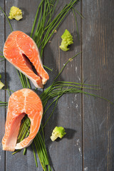 Raw salmon steak and vegetables on wooden dyed background. Top View.