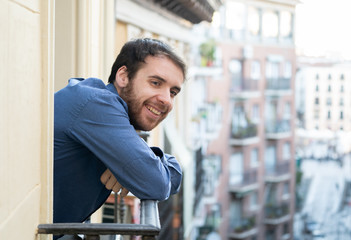 Attractive happy casual young man relaxing at home enjoying the urban view on home balcony