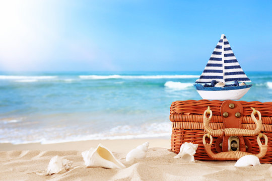 Beach straw suitcase and wooden boat in the sand. Tropical summer vacation concept