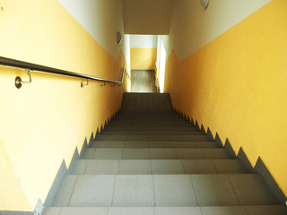 Steep and long stairs down, metal perilla, yellow walls, window below...