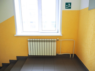 Corridor, window with radiator, yellow painted wall and a sign warning about the stairs. Stairs steps...