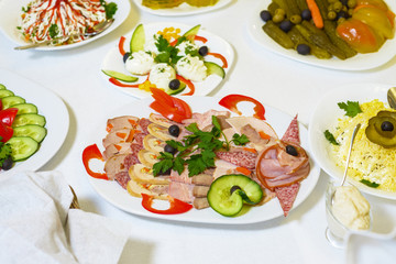 on a serving table food. salad, cucumbers, sausage, pickled vegetables.