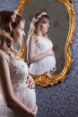 Portrait of a beautiful, young, blond long-haired pregnant mother in a white vintage peignoir, with a floral vink on her head