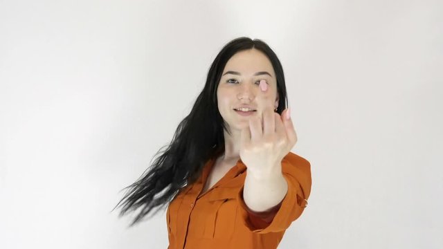 Young woman on a light background. She shows an obscene gesture and smiles.