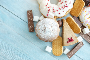 Harmful sweet foods on blue wooden background. Donuts and muffins on the table pile. Unhealthy diet and overweight