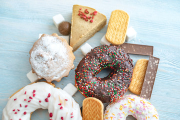 Harmful sweet foods on wooden background. Donuts, muffins, chocolates on the table pile. Unhealthy diet and overweight