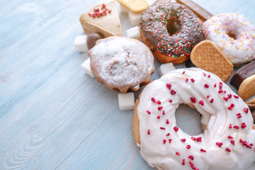 Harmful sweet foods on blue wooden background. Donuts and muffins on the table pile. Unhealthy diet and overweight