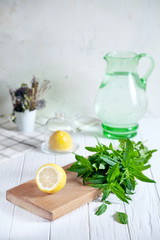 Preparation of the lemonade drink. Cutted lemon on board with fresh mint. Refreshing, cold, summer drink. Lemonade pitcher. Making traditional, healthy lemonade. Ingredients for making mojito