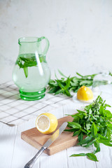 Preparation of the lemonade drink. Cutted lemon on board with fresh mint. Refreshing, cold, summer drink. Lemonade pitcher. Making traditional, healthy lemonade. Ingredients for making mojito