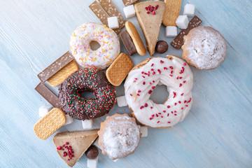 Harmful sweet foods on wooden background. Donuts, muffins, chocolates on the table pile. Unhealthy diet and overweight