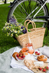 Beautiful summer picnic with strawberries, cheese and rose wine on the lawn in the city park
