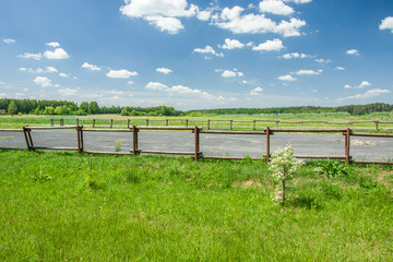 Parking in nature with a wooden fence, trees on the horizon and white clouds on a blue sky