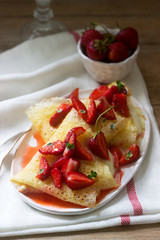 Thin pancakes with cream filling and strawberry sauce on a wooden table. Rustic style.