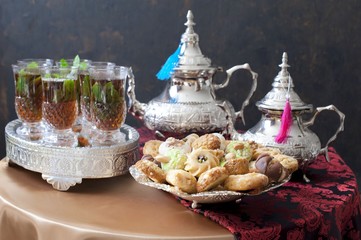 Oriental tea tray and cookies symbolising Moroccan hospitality, Islamic holidays food with decoration. Ramadan kareem. Eid mubarak. Oriental hospitality concept. Tea glasses and pot, traditional delig