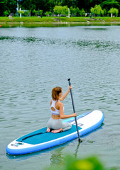 Young girls paddling on SUP board on a calm lake at city. Sup surfing woman. Awesome active training in outdoor.