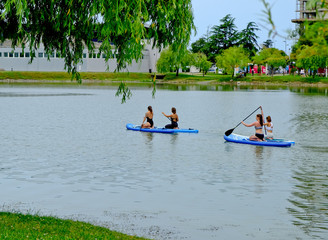 Young girls paddling on SUP board on a calm lake at city. Sup surfing group women. Awesome active training in nature.