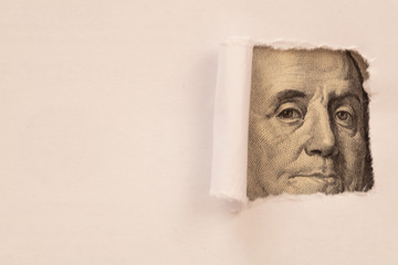 Benjamin Franklin macro peeking through torn white paper
