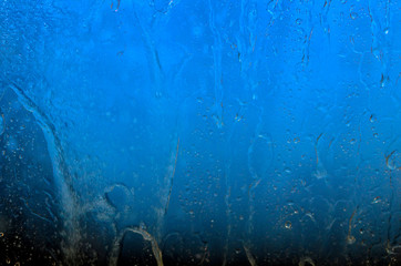 Water flows over the blue glass of the window , background, abstract texture