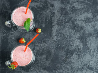Two servings of strawberry smoothie in glass mugs on a dark table