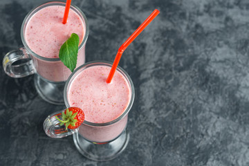 Two servings of strawberry smoothie in glass mugs on a dark table