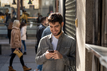 Young attractive happy stylish man on smart phone social network app in european city outdoors