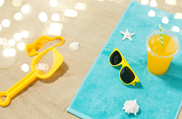 vacation, travel and summer holidays concept - yellow sunglasses, sand toys, seashells and juice drink on beach towel