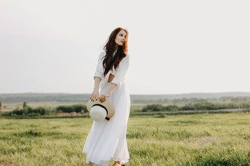 Beautiful carefree long hair asian girl in white clothes and straw hat enjoys life in nature field at sunset. Sensitivity to nature concept