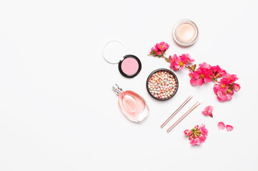 Different makeup cosmetic. Ball blush rouge face powder lipstick concealer bottle of perfume eyeshadow makeup brush spring pink flowers on light background top view flat lay. Beauty fashion background