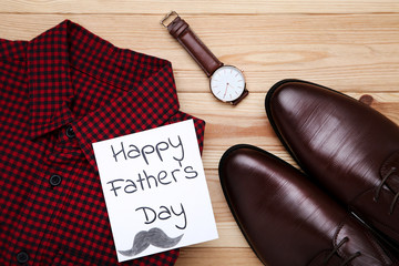 Text Happy Fathers Day with red shirt, male shoes and wrist watch on wooden table
