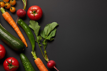 top view of raw tasty vegetables with green leaves on black background with copy space