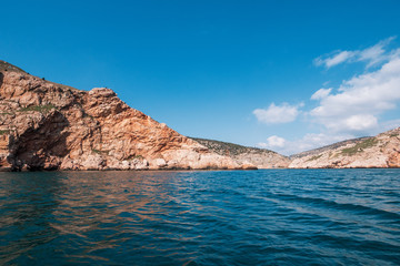 Fototapeta premium Orange island mountain coastline, blue sky with clouds and ocean water, summer travel landscape