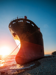 Large iron cargo ship run aground at sea bay at sunset. Industrial sea vessel shipwreck on...