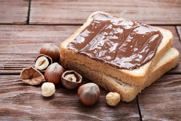 Bread with melted chocolate and hazelnuts on wooden table