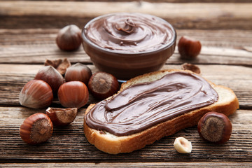 Bread with melted chocolate and hazelnuts on brown wooden table