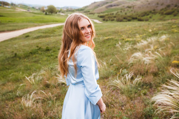 Fototapeta na wymiar Young long-haired girl in a blue dress on a beautiful summer field.