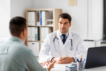 medicine, healthcare and people concept - doctor talking to male patient at medical office in...