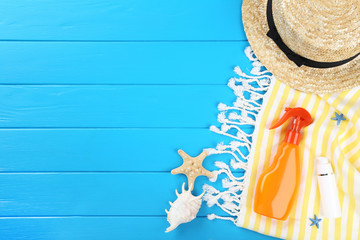 Fototapeta na wymiar Sunscreen bottle with seashells, hat and towel on blue wooden table