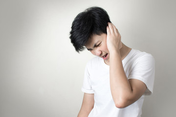 Asian girl with earache that hurts her head isolated on gray background.