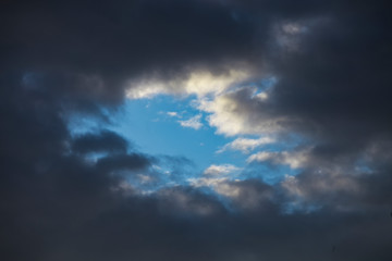 Obraz premium Storm clouds in the blue sky. Darkness and light. Good and evil. Heaven and hell. A piece of blue on the stormy sky background.