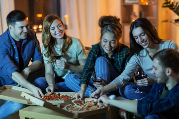 friendship, food and leisure concept - happy friends eating pizza and drinking non-alcoholic wine...