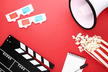 Clapper board with popcorn, megaphone and glasses on red background