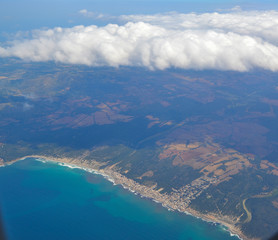 Aerial view from plane window on part of our planet. View on blue sea and beaches with fields. Part of Spain. Memory card from vacation. Big white clouds and earth look. 