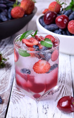 Lemonade with cherries, honeysuckles, strawberries, red syrup and ice in a glass topped with mint on the white table