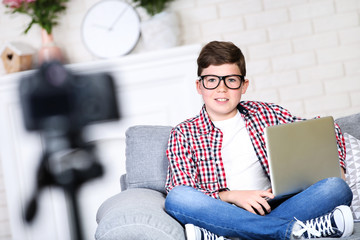 Young boy with laptop sitting on sofa and records video