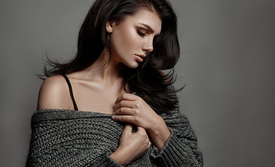 Close-up photo of young charming brunette woman in cozy woolen sweater over gray background.