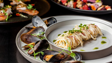 The concept of Italian cuisine. Pasta with cream sauce, pesto and seafood, mussels. European cuisine. Serving dishes in the restaurant with microgreen. copy space