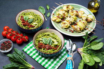 Pasta with spinach creamy sauce, sun-dried tomatoes and cheese. Next rolls of zucchini, with chicken and cheese under spices and herbs.  Selective sharpness, shallow depth of field. Author's retouch