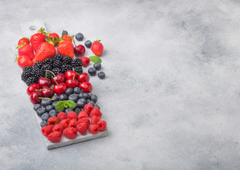 Fresh organic summer berries mix on white marble board on light kitchen table background. Raspberries, strawberries, blueberries, blackberries and cherries. Space for text