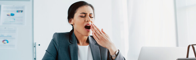 Fototapeta premium panoramic shot of tired latin businesswoman yawning with closed eyes in office